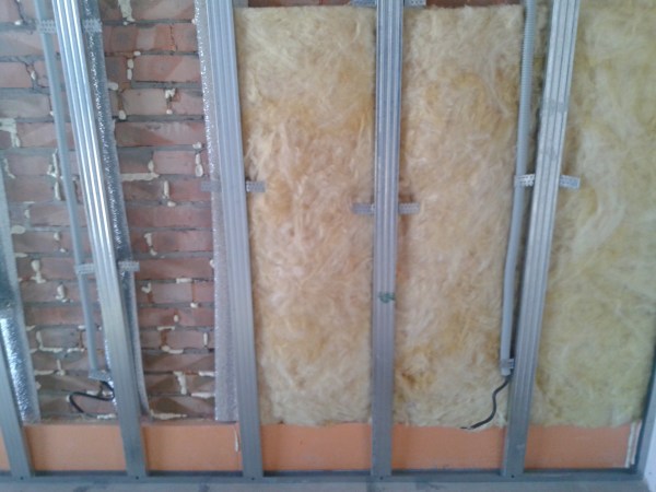 A foto mostra o isolamento e o revestimento de uma parede de tijolos com drywall usando a construção de um perfil de metal