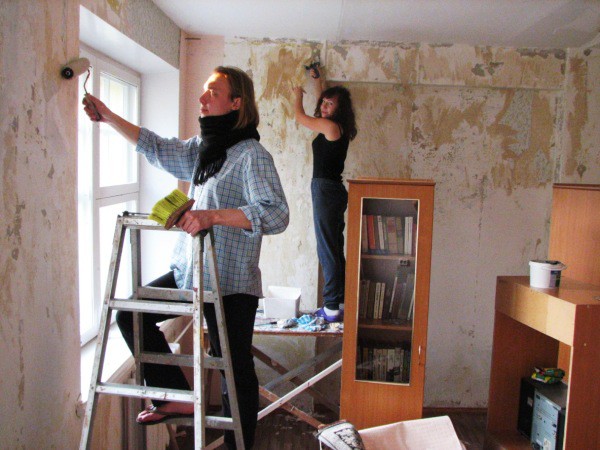 Bildet viser prosessen med å rengjøre veggene og påføre en spesiell beskyttende sammensetning av huset med egne hender