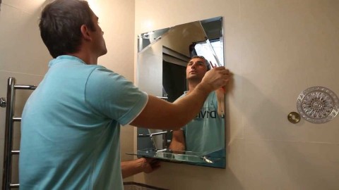 Nous voyons le processus de montage d'un miroir sans cadre sur le mur de la salle de bain.